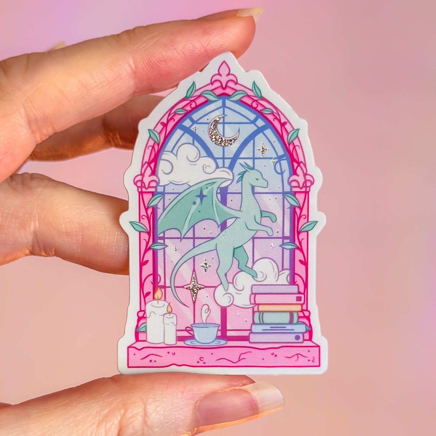 Sticker of a dragon in a stained glass window held by a hand on a pink background