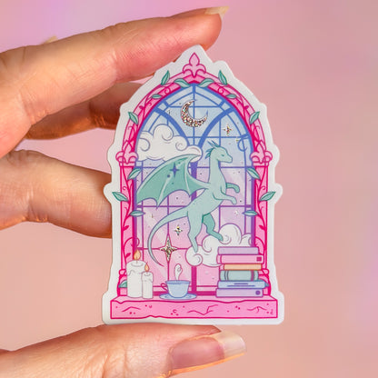 Sticker of a dragon in a stained glass window held by a hand on a pink background