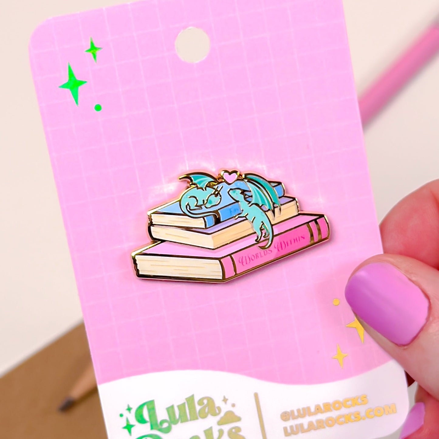 Pin with a dragon design on a pink card held by a hand.