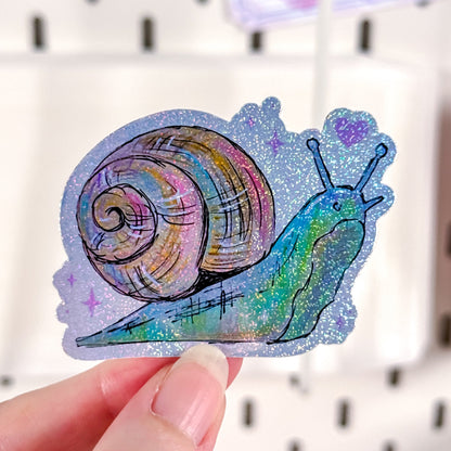 Colorful glittery snail sticker held by a hand against a white background