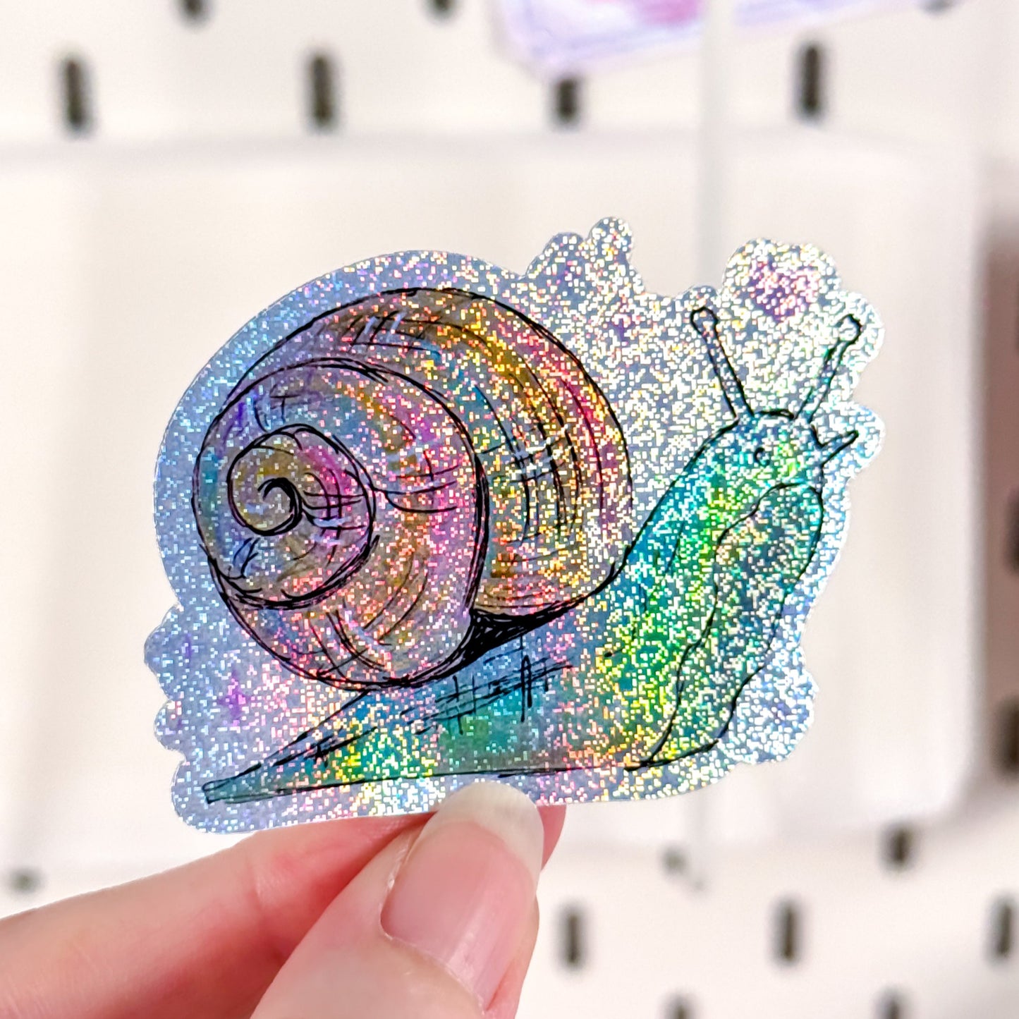 Colorful glittery snail sticker held by a hand with a blurred background