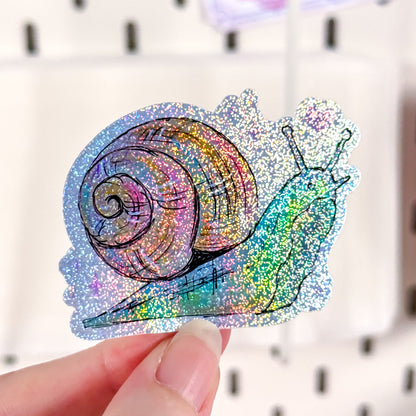 Colorful glittery snail sticker held by a hand with a blurred background