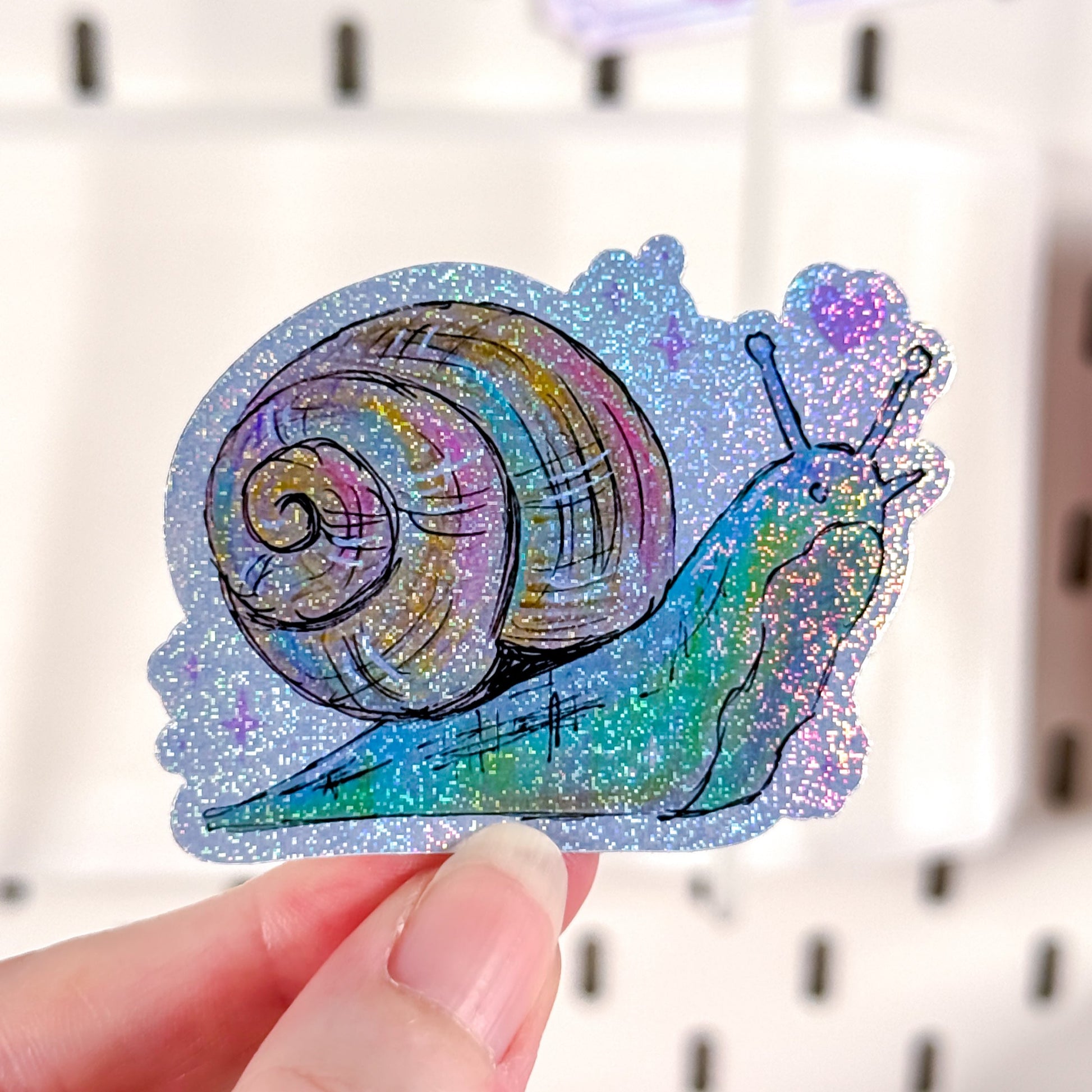 Colorful glittery snail sticker held by a hand with a white background
